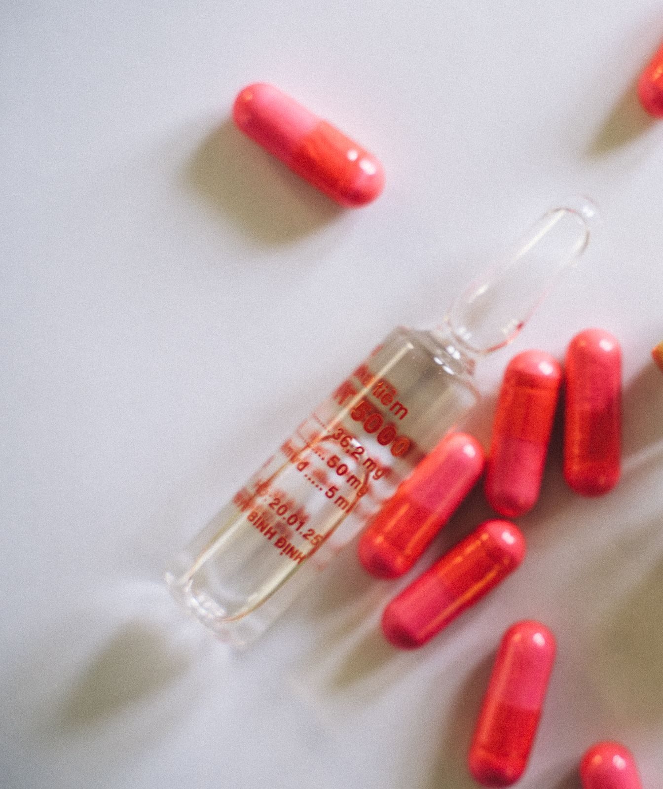 Red capsules, a glass ampoule and an injection vial on a white surface.